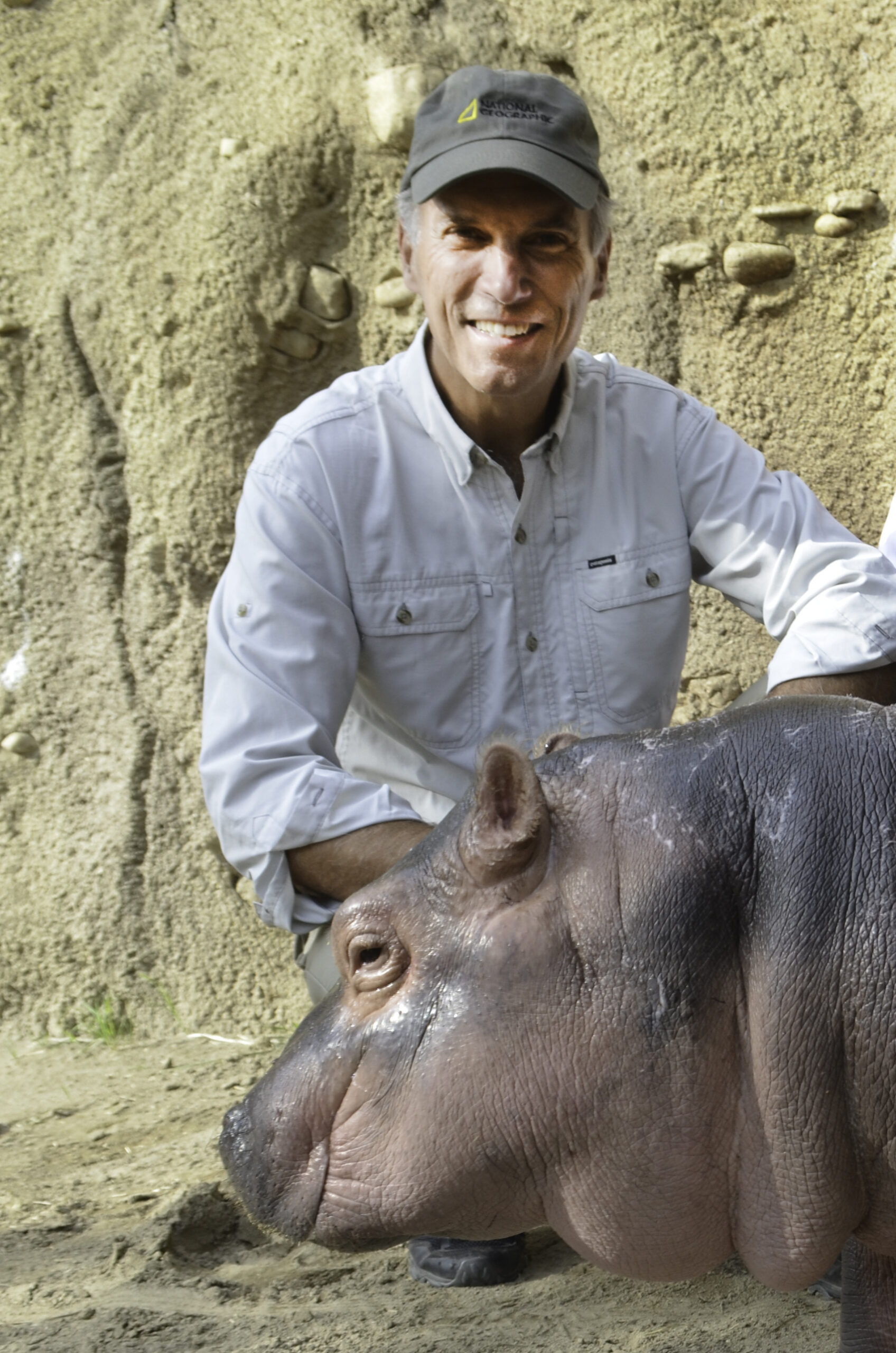 Thayne Maynard of the Cincinnati Zoo kneeling beside a baby hippo, Fiona, highlighting his support for Building Value’s sustainability mission.